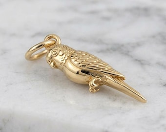 May include: A gold-toned metal charm shaped like a small bird, featuring detailed engravings of feathers on the wings and body, a defined beak, and a circular jump ring attached to the top for hanging on a necklace or bracelet chain.