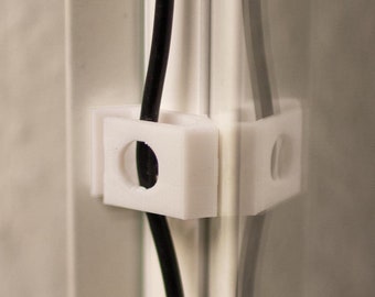 Może przedstawiać: Białe plastikowe zaciski kablowe przymocowane do szklanej powierzchni, utrzymujące czarny kabel na miejscu.