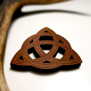 May include: A brown wooden Celtic knot, also known as a Trinity knot, is a decorative design with three interlocked loops. The knot is carved from wood and has a dark brown colour.