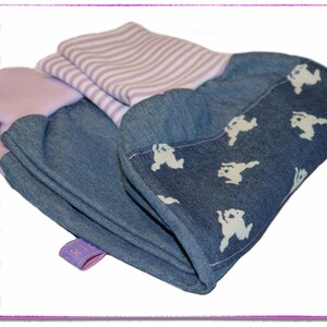 Pu&ograve; includere: Un tessuto di jeans piegato con una stampa bianca di piccoli animali e un tessuto a righe viola e bianco sotto. Il tessuto ha un'etichetta che dice "Spielkidz".