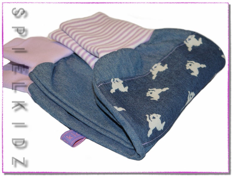 Pu&ograve; includere: Un tessuto di jeans piegato con una stampa bianca di piccoli animali e un tessuto a righe rosa e bianco sotto. Il tessuto ha un'etichetta che dice "Spielkidz".
