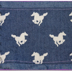 Pu&ograve; includere: Tessuto denim blu con un motivo a cavallo bianco. Il tessuto ha una texture sottile e un colore blu chiaro.