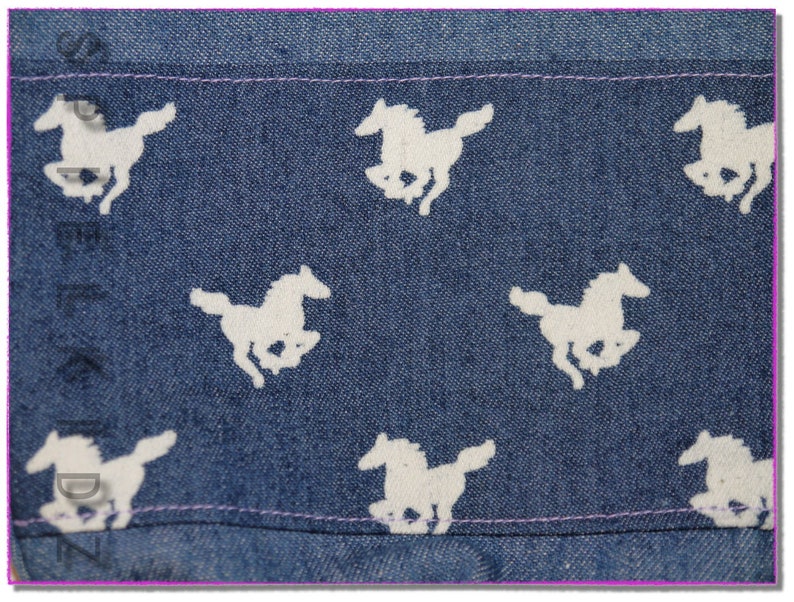 Pu&ograve; includere: Tessuto denim blu con un motivo a cavallo bianco. Il tessuto ha una texture sottile e un colore blu chiaro.