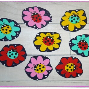Könnte beinhalten: Acht Filzblumenformen mit Marienkäfern in der Mitte. Die Blumen sind in verschiedenen Farben, darunter rosa, rot, gelb und blau. Die Marienkäfer haben schwarze Punkte und befinden sich auf einem dunkelblauen Hintergrund mit weißen Punkten.