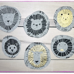 Könnte beinhalten: Sechs graue Stoffkreise mit schwarzen und goldenen Löwenköpfen darauf gedruckt. Die Löwenköpfe haben unterschiedliche Ausdrücke und Details.