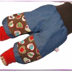 Könnte beinhalten: Babyhose mit jeansblauen Beinen und einem braunen Bund. Die Bündchen haben einen braunen Stoff mit Herz- und Froschmotiven. Rote Fußsocken sind sichtbar. Die Hose ist auf Komfort und Stil ausgelegt.