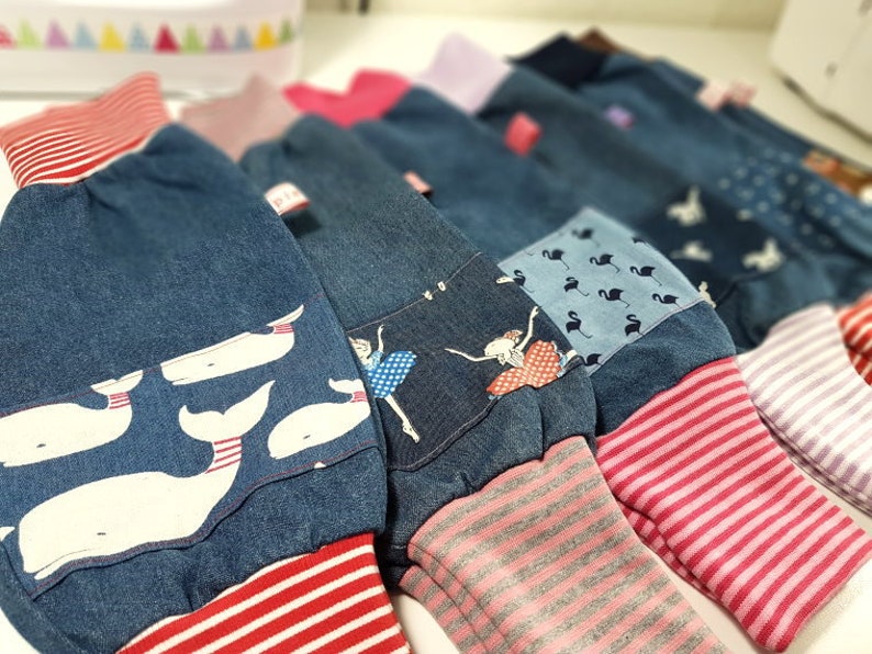 Pu&ograve; includere: Una collezione di pantaloni di jeans con diverse toppe di tessuto stampato colorato e polsini a righe. I pantaloni presentano disegni di balene, ballerine e fenicotteri.