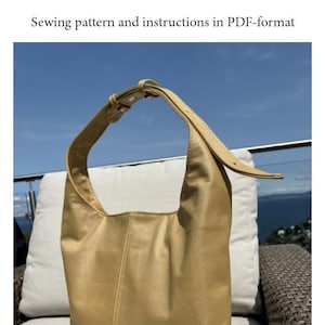 Könnte beinhalten: Gezeigt wird eine beige Ada-Tasche mit Schulterriemen. Die Tasche ist ca. 27 cm hoch, 34 cm breit und 10 cm tief. Das Bild enthält auch den Text "URK! Ada" und "Schnittmuster und Anleitungen im PDF-Format."