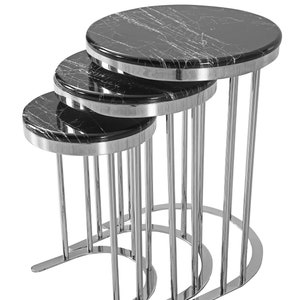 May include: Set of four nesting tables with black marble tops and silver metal frames. The tables are arranged in a staggered formation, with the largest table at the back and the smallest table at the front.