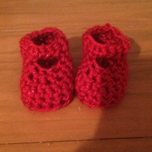 May include: A pair of red crocheted baby booties with a heart-shaped design.