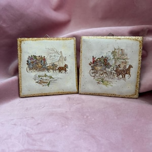 Può includere: Due piastrelle decorative quadrate con illustrazioni vintage di carrozze trainate da cavalli. Le piastrelle hanno uno sfondo color crema con scene dettagliate e un bordo strutturato color beige. Le illustrazioni raffigurano persone in carrozze e cavalli.