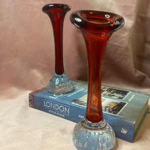 May include: Two vintage glass vases. The vases have a flared, reddish-brown top and a long, slender neck. The base is a light blue with a textured, bubble-like design. The vases are displayed on a book with the word "LONDON" on the cover.