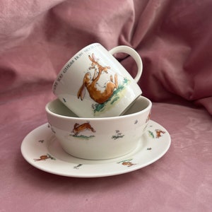 Peut inclure: Un ensemble de tasse, bol et soucoupe en céramique blanche. La tasse et le bol présentent une illustration de lièvre brun et blanc avec le texte "I love you guess how much". La soucoupe et le bol ont un motif de lièvre assorti.