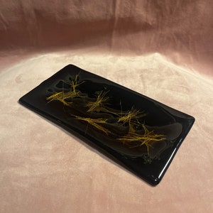 May include: A rectangular black glass tray with gold abstract designs. The tray has a glossy finish and raised edges. The design resembles dried grass or wheat. The tray is likely for decorative use. The dimensions are in centimetres.