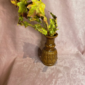 Peut inclure: Un vase en céramique marron avec un motif texturé contient une collection de feuilles séchées. Les feuilles présentent un mélange de teintes vertes, jaunes et brunes. Le vase a une forme bulbeuse avec un col étroit, et mesure environ 15 cm de haut.