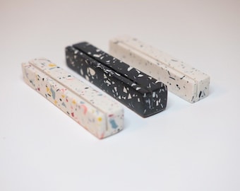 Puede incluir: Tres porta tarjetas de terrazo en diferentes colores: blanco con motas multicolores, negro con motas blancas y blanco con motas negras.