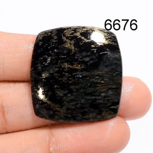 May include: A polished, square-shaped black gemstone with rounded corners, featuring intricate gold-coloured metallic veining throughout its surface. The stone is marked with the number 6676 in the upper right corner, displaying a smooth, reflective finish.