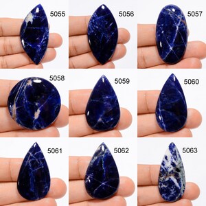 Op de afbeelding: Twaalf cabochon geslepen blauwe en witte sodaliet edelstenen, elk met een uniek patroon en vorm. De stenen zijn genummerd van 5055 tot en met 5063.