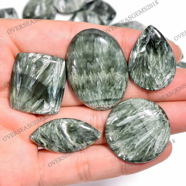May include: Assortment of green and silver gemstone cabochons, including oval, teardrop, and square shapes. The stones have a shimmering, iridescent effect.