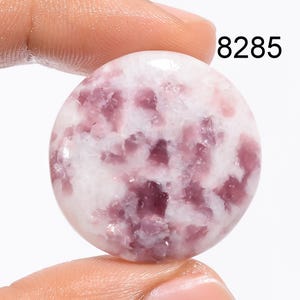 May include: A round, white cabochon gemstone with pink and purple inclusions. The stone is approximately 1 inch in diameter.