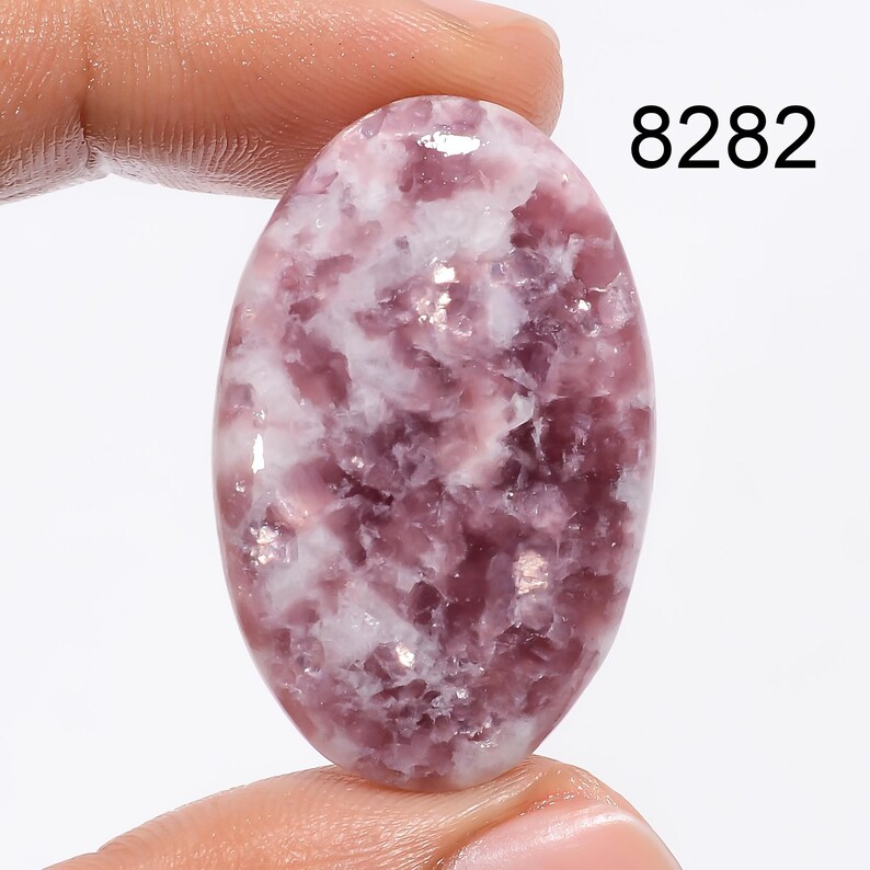 May include: Oval shaped cabochon gemstone with a pink and white pattern. The stone is translucent and has a smooth, polished surface. 8282