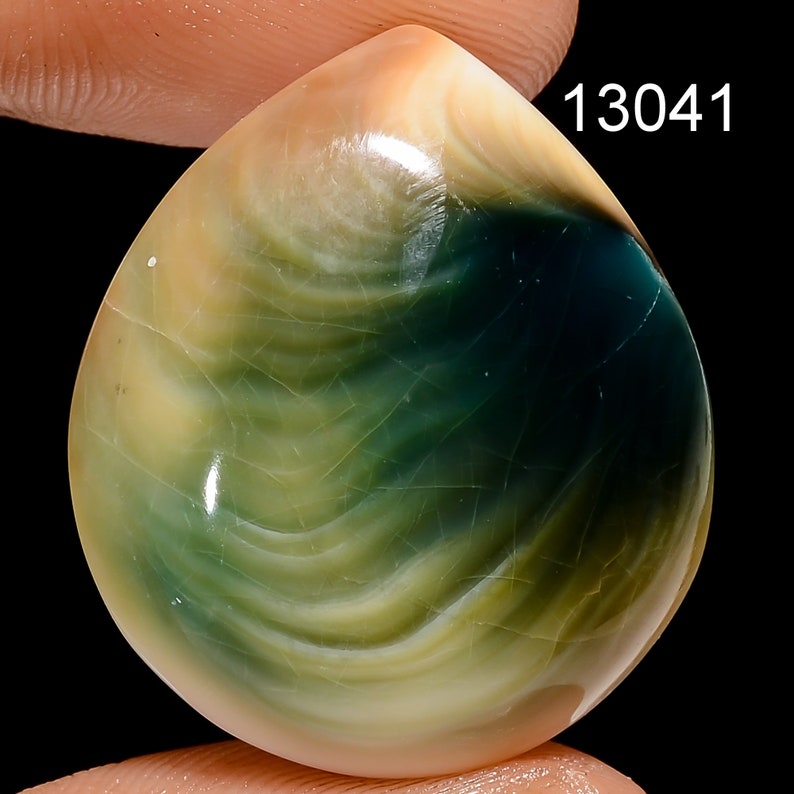 May include: A green, yellow, and white iridescent cabochon gemstone with a teardrop shape. The gemstone is approximately 1 inch in diameter. 13041