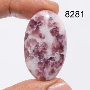 May include: Oval shaped, cabochon cut, pink and white Lepidolite gemstone. The stone has a marbled pattern with a smooth, polished surface.