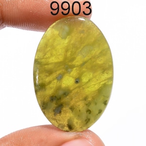 Op de afbeelding: Ovale edelsteen met een geelgroene tint, met donkerdere groene en zwarte insluitsels. Het nummer "9903" is erboven afgedrukt. Het gepolijste oppervlak reflecteert licht en toont een doorschijnende kwaliteit.