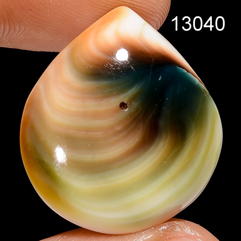 May include: A teardrop-shaped cabochon gemstone with swirling patterns of brown, white, green, and blue. The stone has a smooth, polished surface.