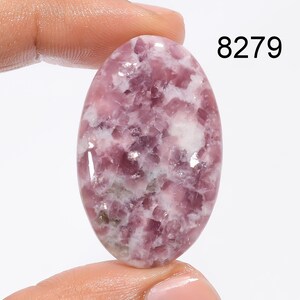 May include: Oval shaped, pink and white Lepidolite cabochon gemstone. The stone has a mottled, cloudy appearance with a smooth, polished surface.