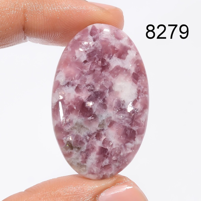 May include: Oval shaped, pink and white Lepidolite cabochon gemstone. The stone has a mottled, cloudy appearance with a smooth, polished surface.