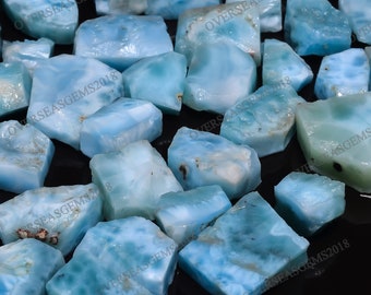 May include: A collection of light blue, white, and gray gemstone chips. The chips are irregularly shaped and have a cloudy, translucent appearance. The chips are scattered on a black surface.