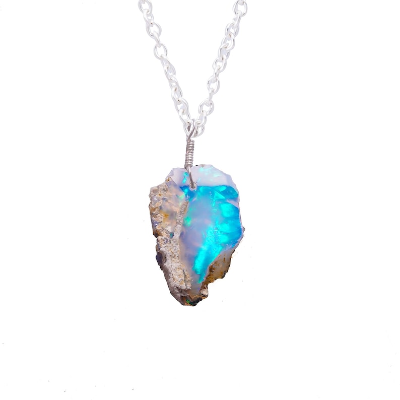 May include: A silver chain necklace with a raw opal pendant. The opal is a light blue color with iridescent flashes of green and white.