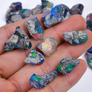 May include: A collection of rough, natural opal stones in various shades of blue, green, and white. The stones are iridescent and have a rough, textured surface.