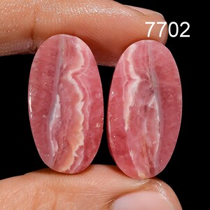 May include: Two oval-shaped pink and white striped cabochons, with a layered pattern, are shown on a finger.