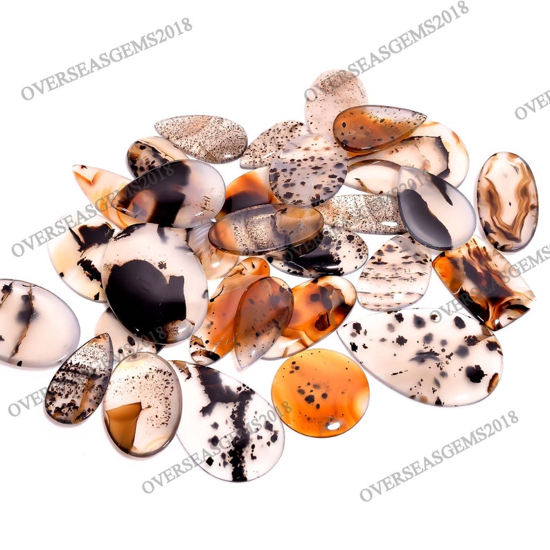 May include: A collection of 20 agate gemstone cabochons in various shades of brown, white, and black. The cabochons are teardrop shaped and have a polished finish.  The cabochons are arranged in a random pattern on a white background.  OVERSEASGEM2018 is printed on the image.
