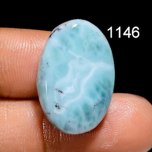 May include: Oval cabochon of blue and white ocean jasper with a swirling pattern and black inclusions. The stone is approximately 1 inch in diameter.