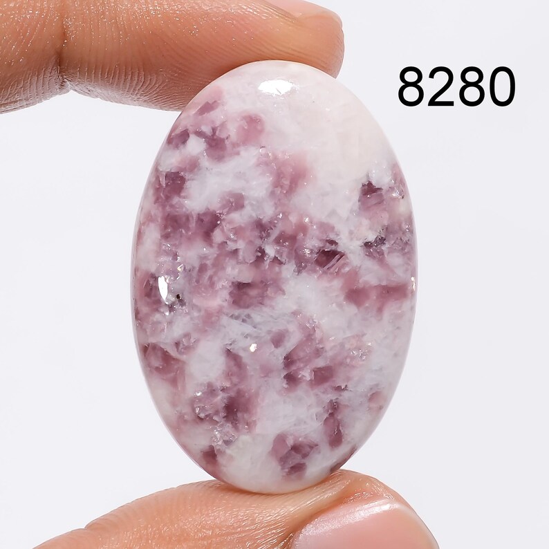 May include: Oval shaped cabochon gemstone with a white and purple color pattern. The stone has a smooth, polished surface. 8280