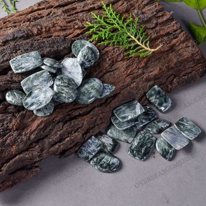 May include: A collection of green and white gemstone cabochons, with a swirling pattern, arranged on a piece of wood.