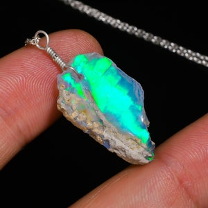 May include: A silver chain necklace with a raw, green and white opal pendant. The opal has a rough, natural texture and displays iridescent colors.