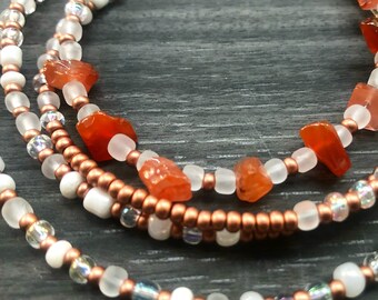May include: A multi-strand beaded bracelet with copper, white, and iridescent beads. The bracelet features orange carnelian gemstone accents.