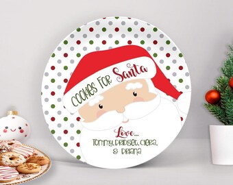 May include: A round white plate featuring a pattern of red and green polka dots. The center displays a cartoon Santa Claus wearing a red hat with the text Cookies For Santa and Love... Tommy, Bridget, Ciera, & Briana printed in red and green.