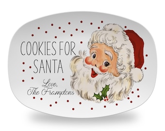 May include: An oval white serving platter featuring a vintage-style illustration of Santa Claus with a red hat and white beard. The text reads COOKIES FOR SANTA and Love, The Framptons. The background is decorated with small red polka dots.