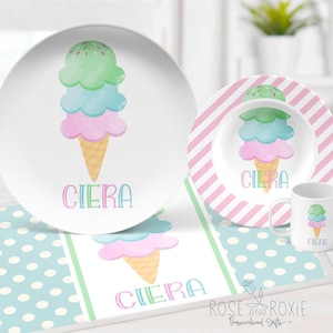 May include: A personalized children's dinnerware set with a pink, blue, and green ice cream cone design. The set includes a large plate, a smaller plate, a bowl, and a mug. The name "Ciera" is printed on each piece.