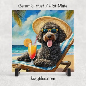 May include: Ceramic trivet or hot plate featuring a black dog wearing sunglasses and a straw hat, relaxing on a beach chair. The dog is enjoying a tropical drink with an orange slice. The background shows a beach scene with palm trees and ocean.