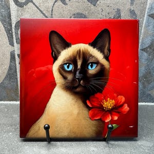Pode incluir: Um gato siamês com olhos azuis e uma flor vermelha em um fundo vermelho.