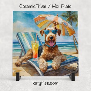 May include: Ceramic trivet featuring a dog wearing sunglasses, relaxing on a beach chair under an umbrella. The dog has a drink with a straw. The background shows a beach scene with palm trees and the ocean. The text "katytiles.com" is at the bottom.
