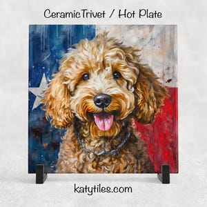 May include: Ceramic trivet featuring a smiling, curly-haired dog with a Texas flag background. The dog has a brown coat and a silver collar. The trivet is displayed on a black stand. The text "katytiles.com" is at the bottom.