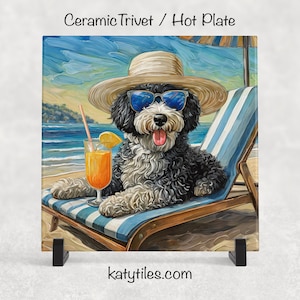 May include: Ceramic trivet featuring a black and white dog wearing sunglasses and a straw hat, relaxing on a beach chair with a drink. The background shows a beach scene with blue water and sky. The text "katytiles.com" is at the bottom.