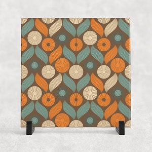 May include: A square ceramic tile with a geometric pattern of overlapping circles and leaves in shades of brown, orange, teal, and cream.